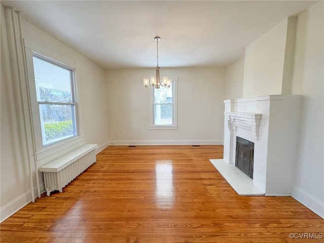 unfurnished living room with light wood-type flooring, a brick fireplace, radiator, a notable chandelier, and a wealth of natural light