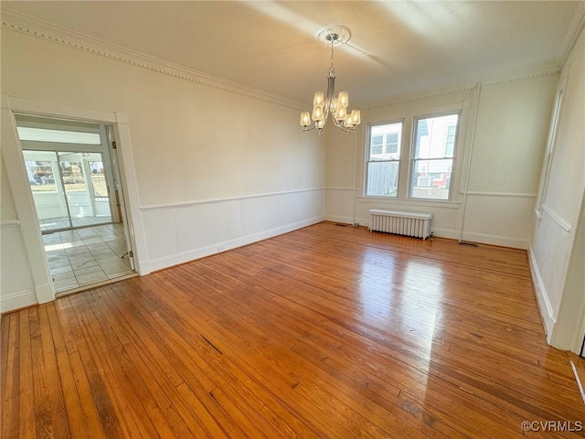 spare room featuring radiator, crown molding, an inviting chandelier, and hardwood / wood-style flooring