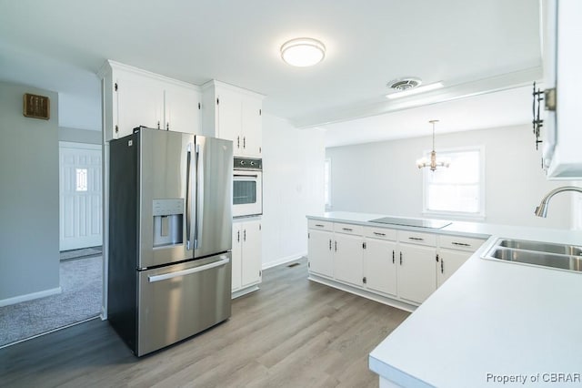 kitchen featuring sink, white cabinetry, oven, stainless steel fridge, and hanging light fixtures