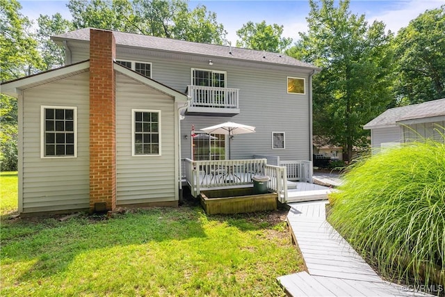 rear view of property featuring a balcony, a wooden deck, a lawn, and a chimney