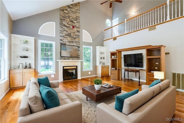 living area featuring light wood-style flooring, baseboards, visible vents, a fireplace, and ceiling fan