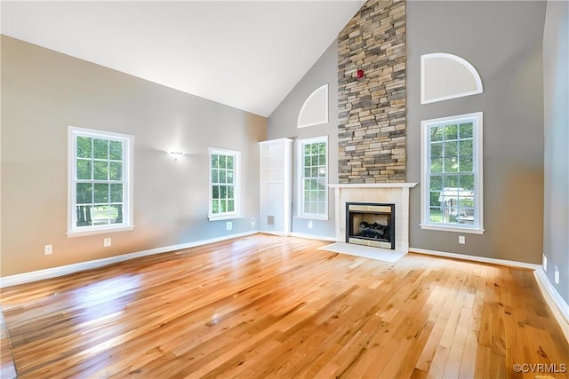 unfurnished living room with baseboards, a stone fireplace, light wood finished floors, and high vaulted ceiling