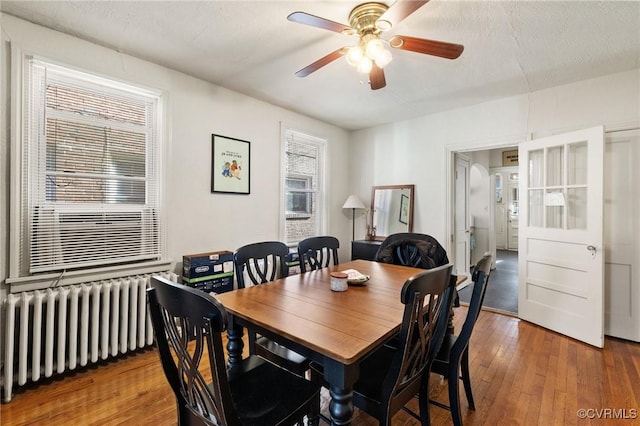 dining space with radiator heating unit, ceiling fan, a textured ceiling, and wood finished floors