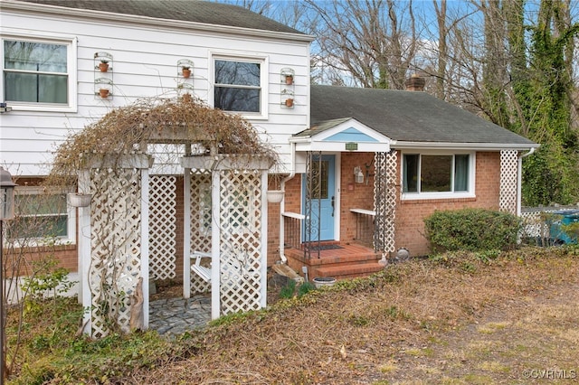 view of front of property with a shingled roof, brick siding, and a chimney