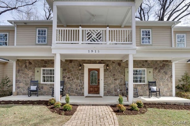 entrance to property featuring a balcony, stone siding, and a porch