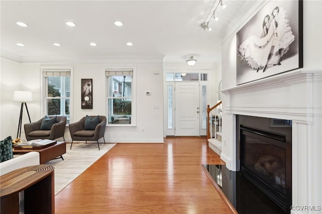 living room with light wood-style floors, recessed lighting, a glass covered fireplace, and crown molding