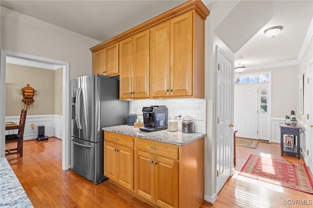 kitchen featuring light stone counters, wainscoting, stainless steel fridge, and light wood-style flooring