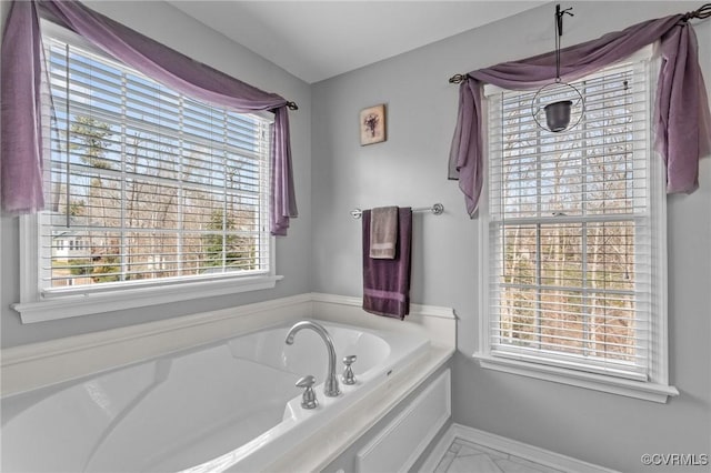 bathroom with marble finish floor, a garden tub, and baseboards