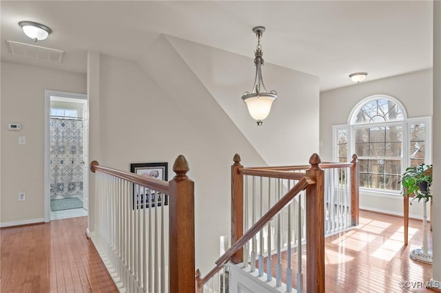 hallway with visible vents, wood-type flooring, an upstairs landing, and baseboards