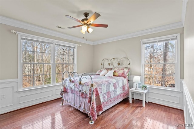 bedroom featuring a wainscoted wall, wood-type flooring, visible vents, and ornamental molding