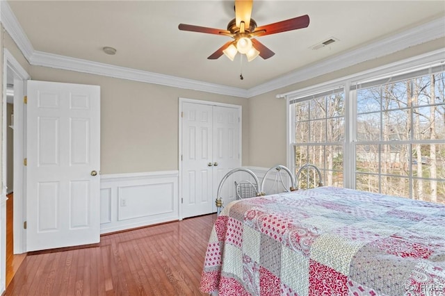 bedroom featuring wood finished floors, visible vents, ornamental molding, a closet, and wainscoting