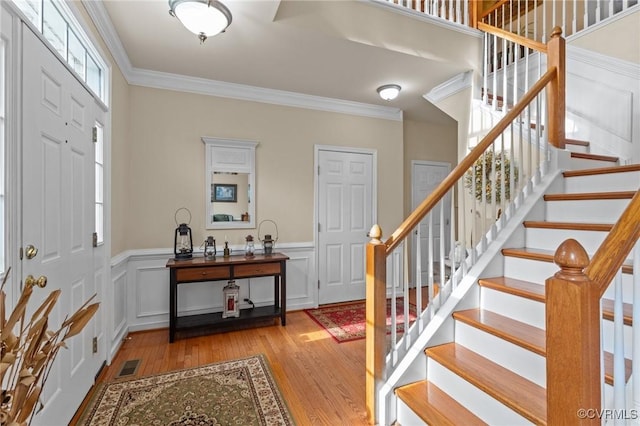 entrance foyer with light wood-style floors, visible vents, a decorative wall, and crown molding