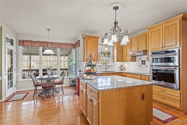 kitchen featuring decorative backsplash, light wood-style floors, stainless steel double oven, a sink, and light stone countertops