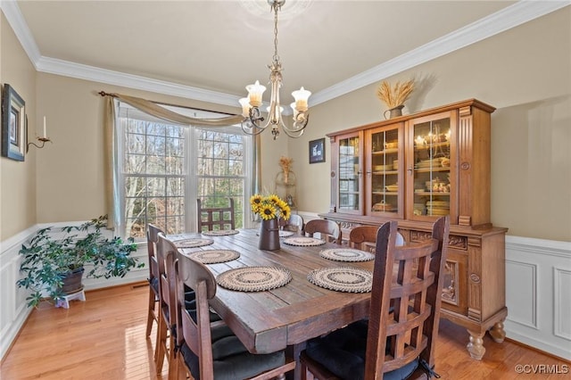 dining space with light wood-style floors, ornamental molding, and wainscoting