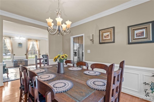 dining room with crown molding, light wood-style floors, wainscoting, and an inviting chandelier