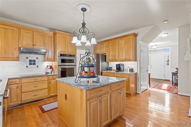 kitchen with decorative backsplash, light wood-style flooring, appliances with stainless steel finishes, light stone countertops, and under cabinet range hood