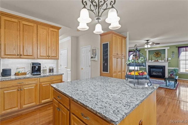 kitchen with light stone counters, a glass covered fireplace, light wood-style flooring, and tasteful backsplash