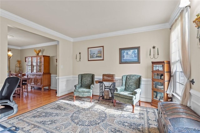 living area with a wainscoted wall, crown molding, an inviting chandelier, and wood finished floors