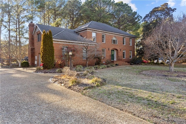 view of front of property featuring brick siding, a chimney, and a front yard