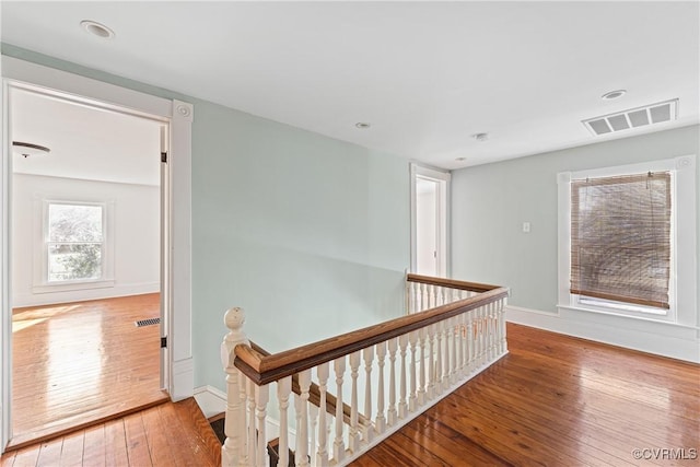 corridor featuring wood finished floors, an upstairs landing, visible vents, and baseboards