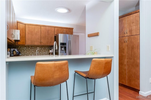 kitchen featuring brown cabinetry, stainless steel fridge with ice dispenser, a breakfast bar, a peninsula, and light countertops