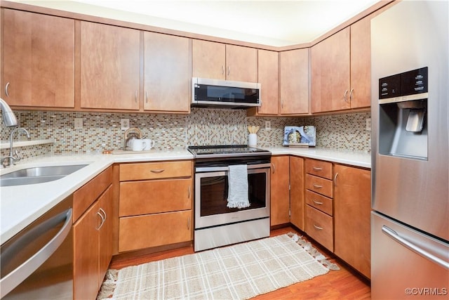 kitchen with light wood finished floors, appliances with stainless steel finishes, backsplash, light countertops, and a sink