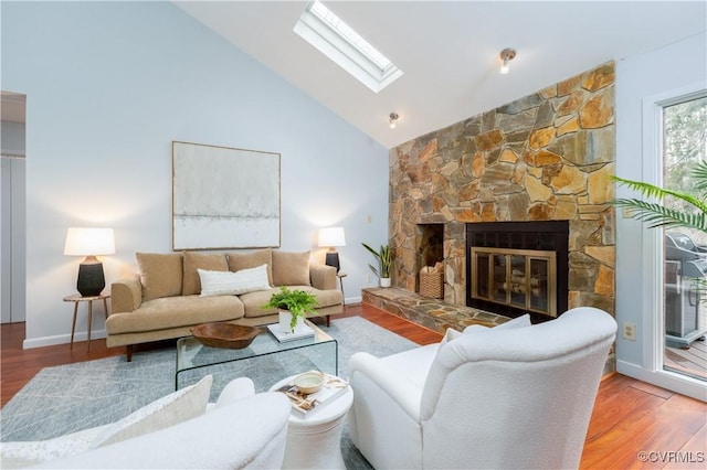 living room featuring a skylight, a stone fireplace, wood finished floors, high vaulted ceiling, and baseboards