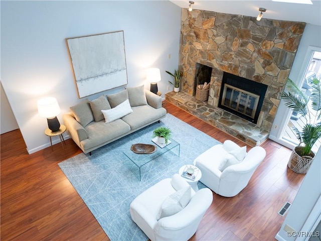 living room with visible vents, baseboards, wood finished floors, and a stone fireplace