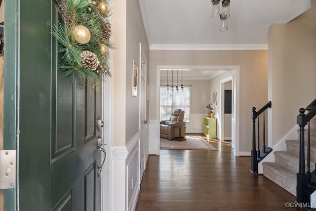 foyer featuring wainscoting, dark wood-type flooring, stairs, crown molding, and a decorative wall