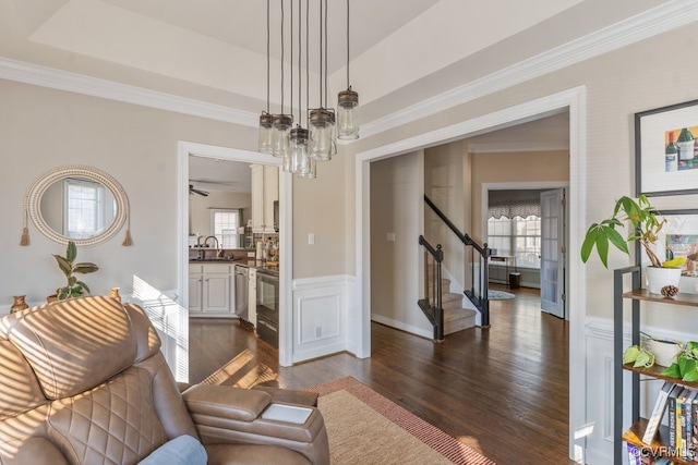 living area featuring dark wood-style floors, ornamental molding, stairway, and a healthy amount of sunlight