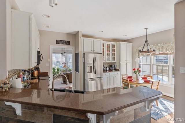 kitchen with stainless steel refrigerator with ice dispenser, hanging light fixtures, glass insert cabinets, a peninsula, and a kitchen breakfast bar