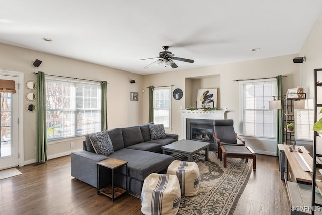 living room featuring a glass covered fireplace, dark wood-style flooring, ceiling fan, and baseboards