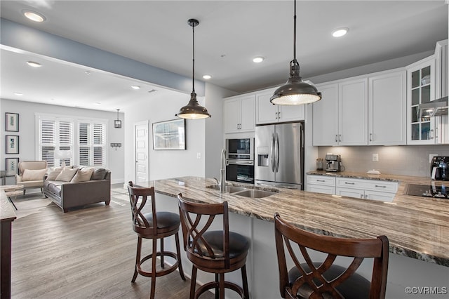 kitchen with light stone counters, appliances with stainless steel finishes, glass insert cabinets, white cabinets, and a sink