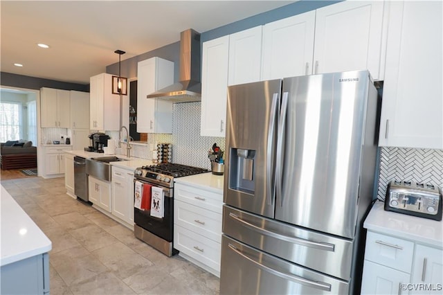 kitchen with appliances with stainless steel finishes, light countertops, hanging light fixtures, and wall chimney range hood