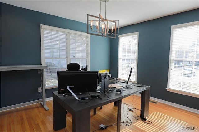 office space with a chandelier, wood finished floors, visible vents, and baseboards