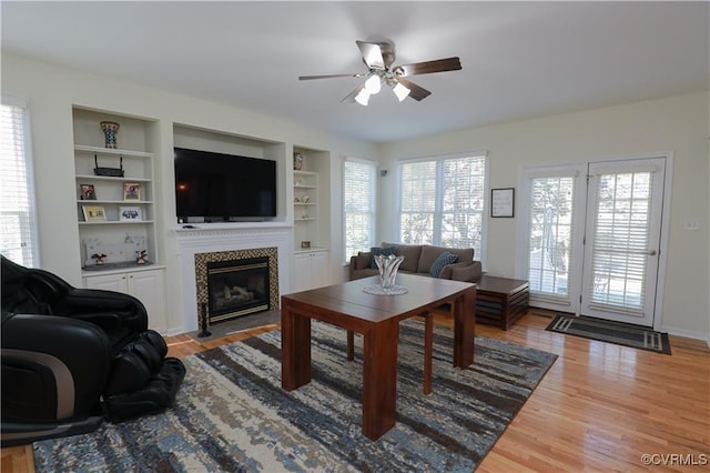 living room featuring built in features, baseboards, ceiling fan, light wood-style floors, and a fireplace