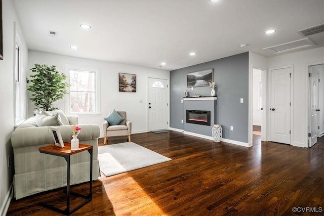 living room featuring dark wood-style floors, recessed lighting, visible vents, a glass covered fireplace, and baseboards