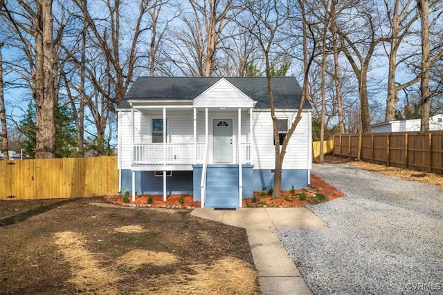 bungalow-style house featuring covered porch, gravel driveway, and fence