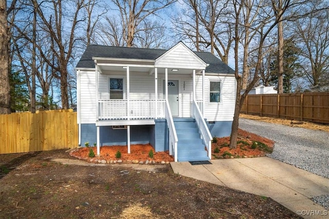 view of front of house featuring driveway, a porch, a chimney, and fence