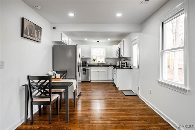 kitchen featuring dark wood-style floors, tasteful backsplash, dark countertops, appliances with stainless steel finishes, and white cabinetry