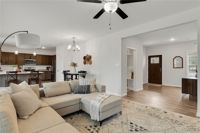 living area featuring recessed lighting, light wood-style flooring, baseboards, and ceiling fan with notable chandelier