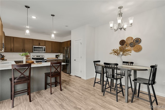 kitchen with light wood-style flooring, a breakfast bar area, decorative light fixtures, stainless steel appliances, and light countertops