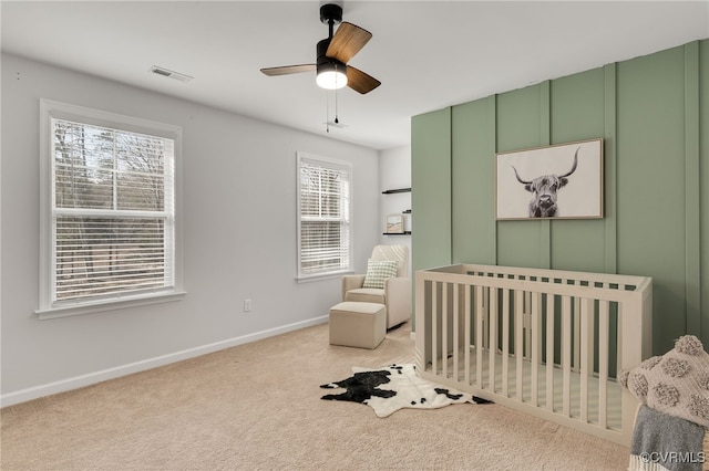 bedroom with light carpet, visible vents, baseboards, ceiling fan, and a nursery area