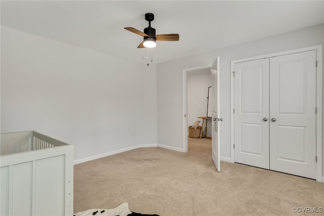 unfurnished bedroom featuring light carpet, ceiling fan, baseboards, and a closet