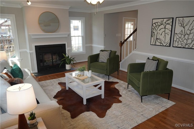 living area featuring a fireplace with flush hearth, stairs, ornamental molding, and wood finished floors