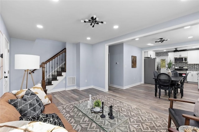 living room with recessed lighting, visible vents, baseboards, stairs, and light wood-style floors