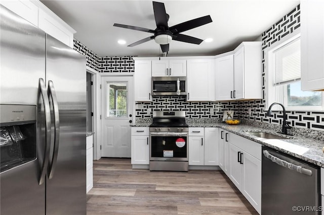 kitchen with light stone countertops, white cabinetry, appliances with stainless steel finishes, and a sink