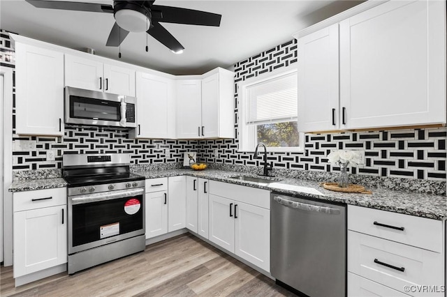 kitchen with white cabinets, light stone countertops, stainless steel appliances, and a sink