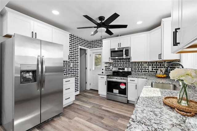 kitchen with white cabinets, light wood-style flooring, appliances with stainless steel finishes, light stone countertops, and backsplash