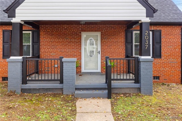 property entrance featuring a shingled roof, a porch, and brick siding